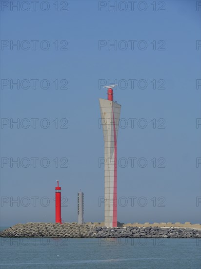 Three lighthouses in red and white on the coast, in front of a blue sky and calm sea, oostende,
