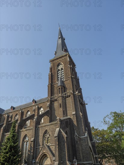 Large Gothic church with high tower and pointed arch windows made of red brick under a clear sky,
