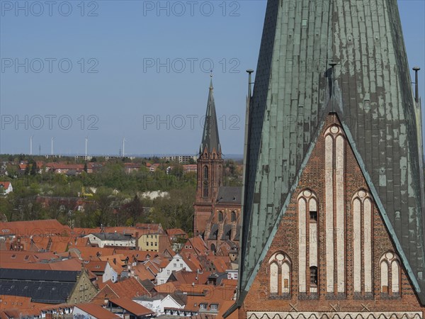 Church towers and roofs of a town, surrounded by landscape and wind turbines in the background,