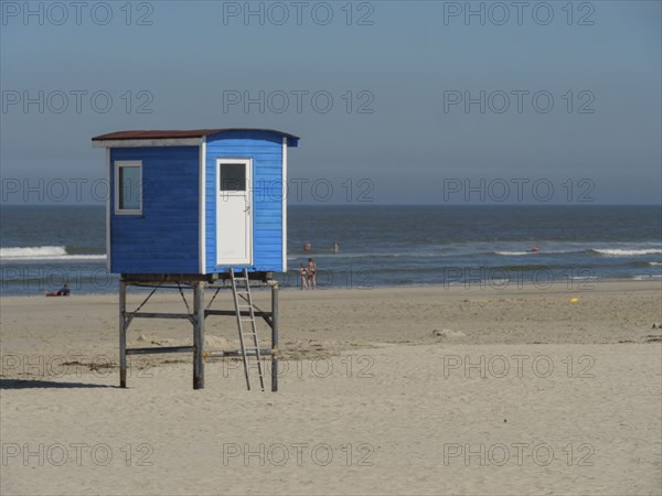 Blue lifeguard tower on sandy beach with calm sea and people in the background, langeoog, germany
