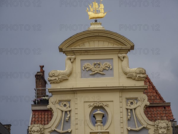 Detailed view of a building gable with golden decorations and a coat of arms. Grey cloudy sky,
