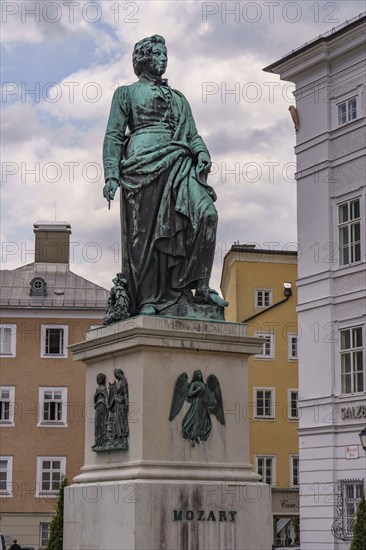 Monument to Mozart on a square surrounded by historic buildings under a cloudy sky, Salzburg,
