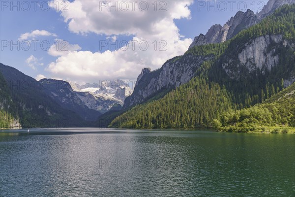 An unspoilt mountain lake, framed by high peaks and dense forests under a cloudy sky, Gosau,