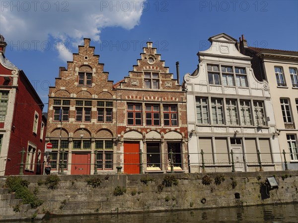 A row of old brick and faÃ§ade buildings along a canal in sunny weather, gent, belgium