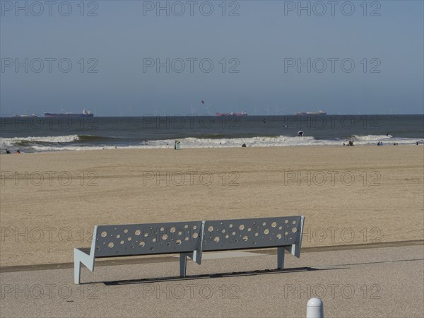 Bench with holes on the beach, in the background the sea and a slightly cloudy sky, scheveningen,