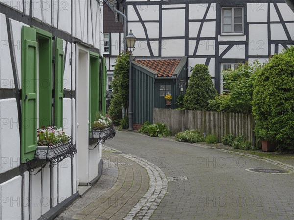 Narrow cobbled street with half-timbered houses and green shutters in a German village, Westerholt,