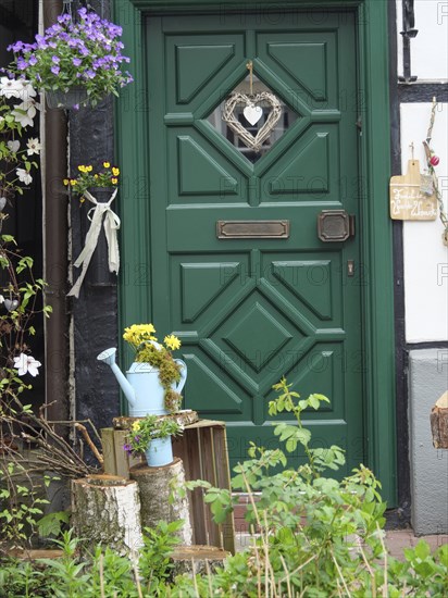 Rustic green door of a half-timbered house, decorated with flowers and a watering can in a