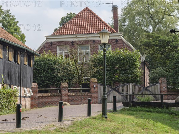 A cosy brick house with an old street lamp and a small bridge in a green garden, haaksbergen, .