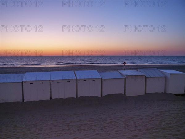 White beach huts at dusk, with an intensely coloured sunset and calm sea, de haan, Belgium, Europe