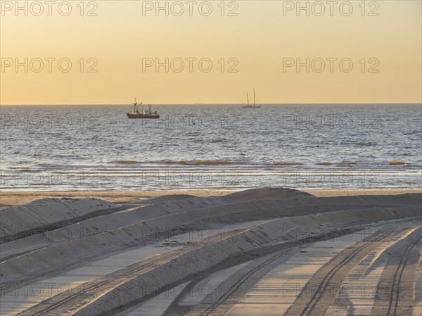 A sunset over the sea with silhouettes of boats and a sandy beach in the foreground, de haan,