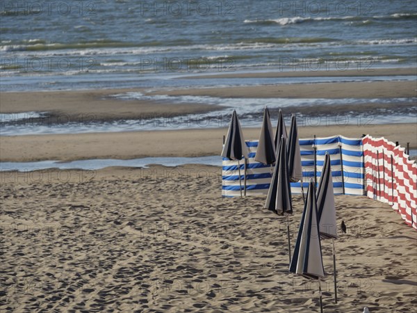 Beach view with blue-white and red-white windbreaks and calm sea in the background, de haan,
