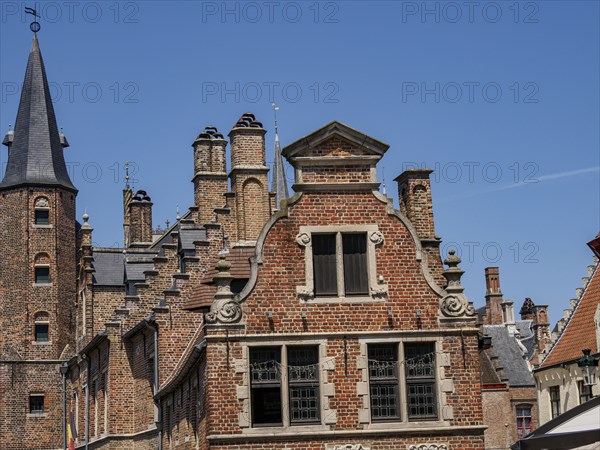 Detailed facades of historic buildings with many bricks and towers under a bright blue sky, Bruges,