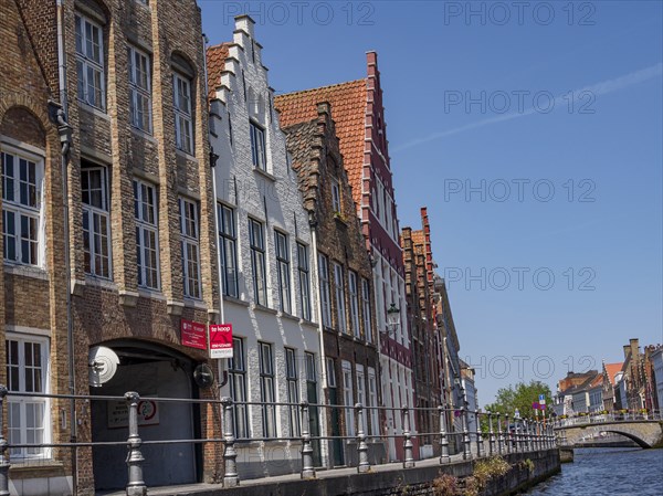 Historic buildings with red roofs and facades on the canal under a blue sky, Bruges, Belgium,