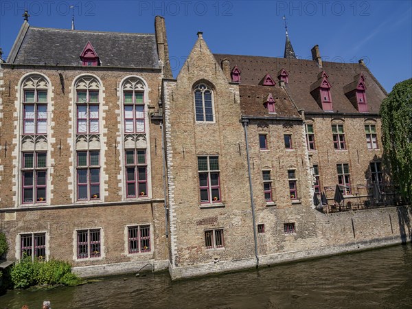 Historic buildings with brick facades along a canal under a bright blue sky, Bruges, Belgium,