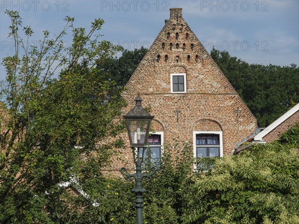 An old house with brick faÃ§ade and windows, surrounded by abundant vegetation and a classic street