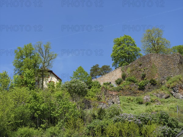 Historic ruin and a small house on a green hill surrounded by lush vegetation under a clear sky,