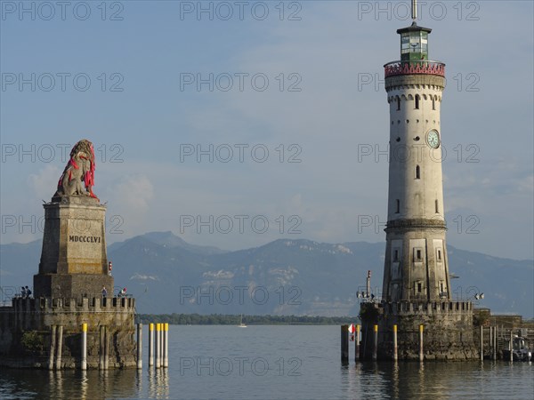 Lighthouse and lion statue at the entrance of a harbour, mountain landscape in the background,