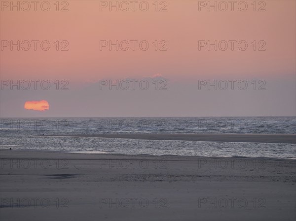 The sun disappears behind the sea on the horizon and colours the sky orange, juist, east frisia,