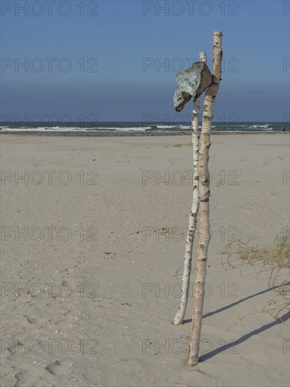 Beach with wooden poles and flag in the sand, sea in the background, blue sky, juist, east frisia,