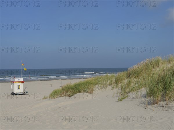 Small hut with flag on a wide sandy beach with dunes and blue sky, Juist, East Frisia, Germany,