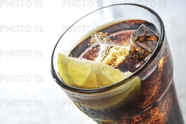 Part of a drinking glass with fresh cola, ice cubes and lemon slice, refreshing sweet caffeine