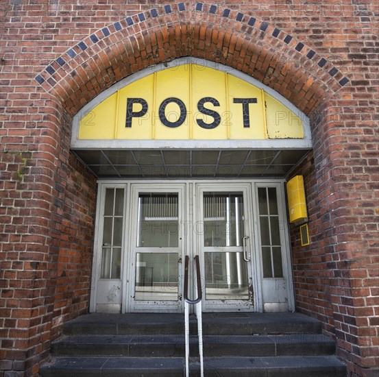 Entrance to the Post office in an historic building with a yellow sign, an old door and an arch of