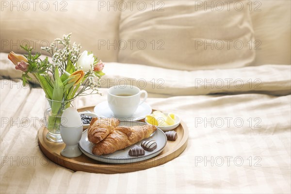 Romantic breakfast in bed with flowers, croissant, coffee cup and hearts from chocolate on beige