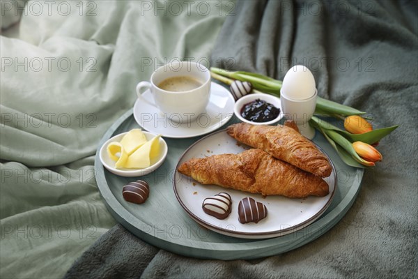 Breakfast served with love in bed, coffee, croissant, jam, egg, some chocolate hearts and tulips on