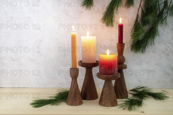 Four candles on wooden stands, all are lit for the fourth Advent, pine branch decoration, light
