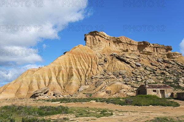 Small hut in front of a striking rocky hill in a desert-like landscape under a blue sky, Bardenas