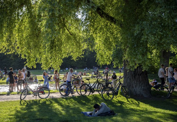 Large meadow at Schwabinger Bach, Many people on a summer day in the English Garden, Munich,