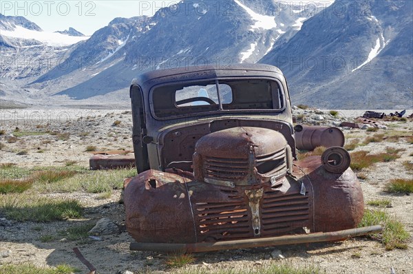 Old, rusty car in a junkyard with a view of mountains and blue sky in the background, remains from