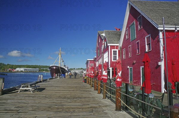 Harbour with red buildings and a boat on the water along a wooden jetty under a blue sky, fishing,