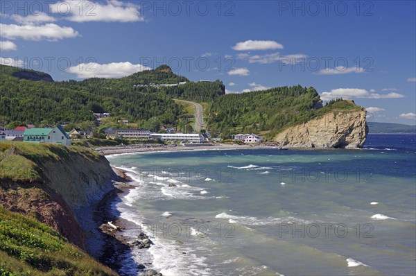 Coastal landscape with hills, cliffs and houses, the sea and waves under a clear blue sky, Perce,