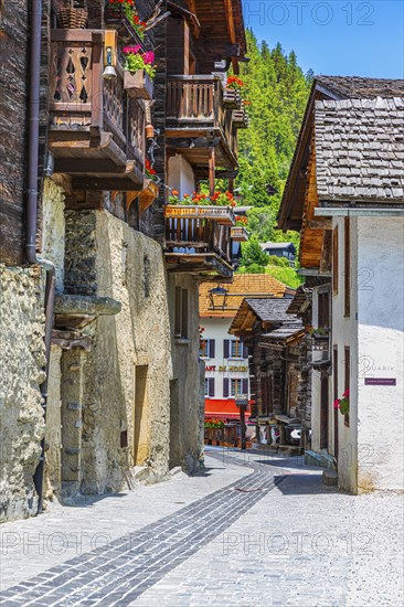 Paved footpath surrounded by old wooden houses, flower boxes on balconies and windows, historic