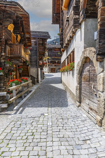 Paved footpath surrounded by old wooden houses, flower boxes on balconies and windows, historic