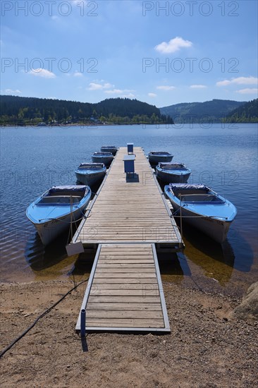 Jetty with moored boats on the Schluchsee, surrounded by mountains and forests, under blue sky,