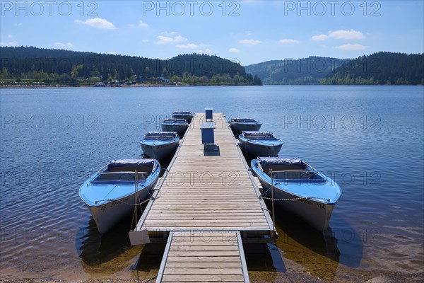 Jetty with moored boats on the Schluchsee, surrounded by mountains and forests, under blue sky,