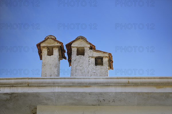 Light plastered chimneys with tiled roofs on a building in Greece, looking like little houses, blue
