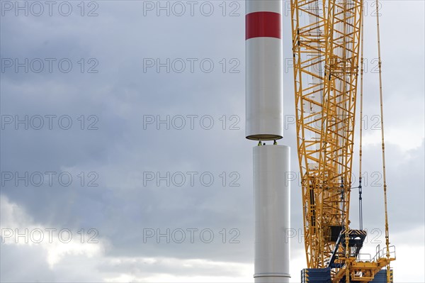 Crane is moving a tower part of a wind turbine onto the first tube guided by people inside,