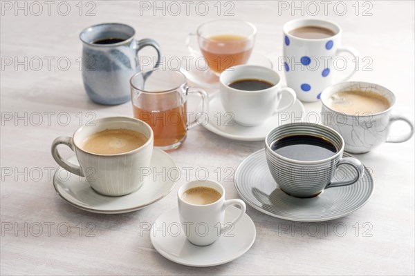 Group of different cups and mugs with coffee and tea drinks on a light table, selected focus,