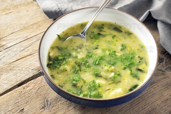 Potato parsley soup in a plate with spoon on a rustic wooden table, healthy vegetarian dish, copy