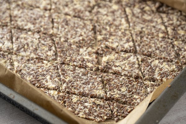 Baking tray with dough from linseed, oat flakes and cheese, cut into rhombs to make healthy crispy