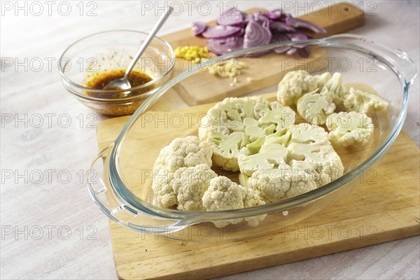 Raw cauliflower slices in a glass casserole, chopped red onion and a spice mix in olive oil,