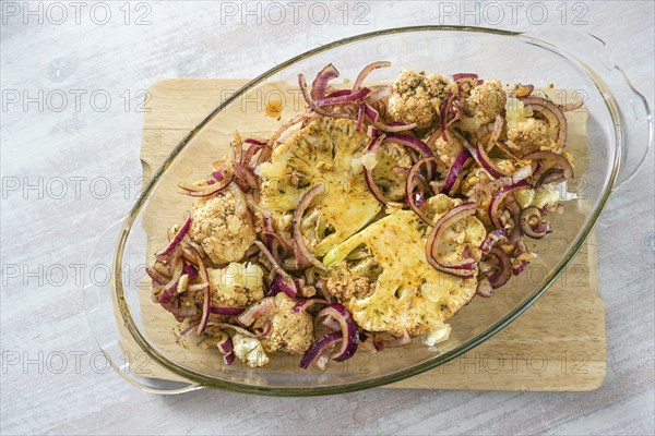 Baked cauliflower steaks with spicy oil and red onions in a glass casserole on a wooden kitchen