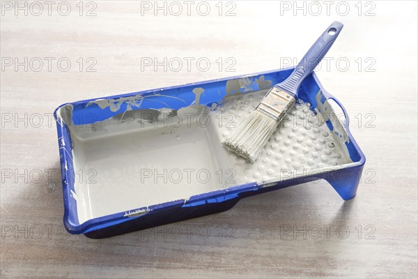 Blue paint tray with light gray lacquer and a brush on a wooden table, craft concept for