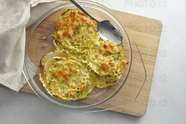 Gratinated slices of Chinese or napa cabbage in a glass casserole on a wooden kitchen board,