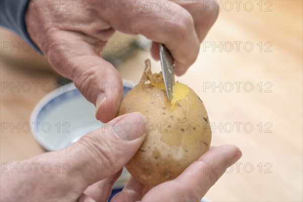 Hands of an elderly man peeling a cooked potato with a kitchen knife, preparing food, copy space,