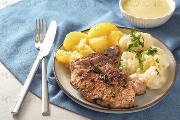 Dish with pork chop, cauliflower, potatoes and hollandaise sauce served with herb garnish on a