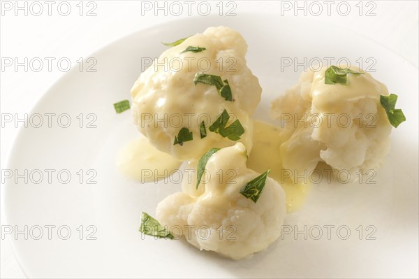 Cooked cauliflower with hollandaise sauce and parsley garnish on a white plate, vegetable side